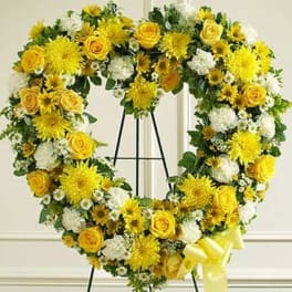 Heart-shaped standing wreath of yellow roses and white flowers with yellow bow on an easel