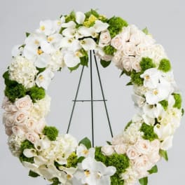 Large wreath of white orchids, calla lilies, hydrangeas and blush roses on a metal easel stand