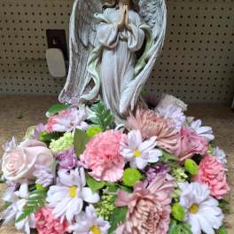 Angel figurine surrounded by a low mound of pink and white flowers.