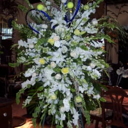 Large white floral standing arrangement with blue tennis rackets and tennis balls