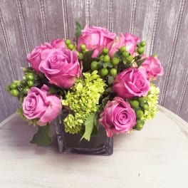 Pink roses arranged in a square glass vase with green accents