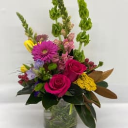 Mixed bouquet with pink roses, purple daisies, and tall green spikes in a glass vase