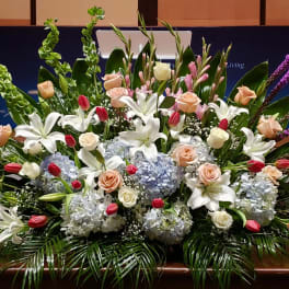 Large front-facing arrangement of white lilies, peach roses, blue hydrangeas, and pink tulips