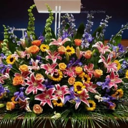Large altar arrangement of pink lilies, orange roses, yellow sunflowers, and blue delphinium