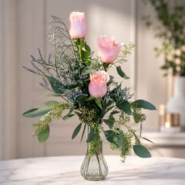 Three pink roses in a clear glass vase with airy purple filler