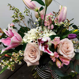 Bouquet of pink lilies, pale roses, and white filler flowers in a glass vase