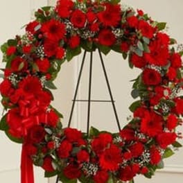 Standing wreath of red flowers with white accents on a black metal easel with red ribbon