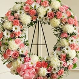 Large round wreath of pink roses and white mums on an easel with a pink bow