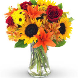 Bouquet of sunflowers, red roses, and orange lilies in a glass vase