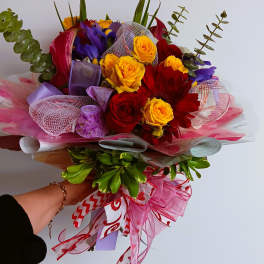 Handheld bouquet of red, yellow, and purple flowers with pink ribbon wrap