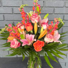 Mixed bouquet of pink roses, lilies, and orange snapdragons in a glass vase