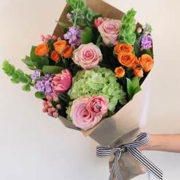 Hand-tied bouquet of pink, orange, and green flowers wrapped in paper