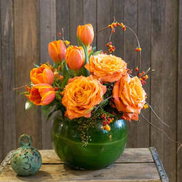 Orange tulips and roses arranged in a green glass vase