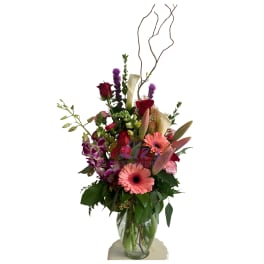 Tall mixed bouquet with pink gerberas, red roses, and purple orchids in a glass vase