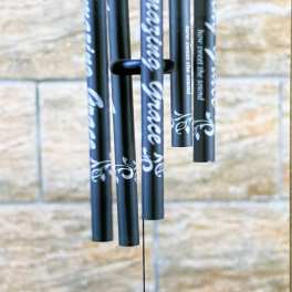 Black wind chime with silver text hanging against a stone wall