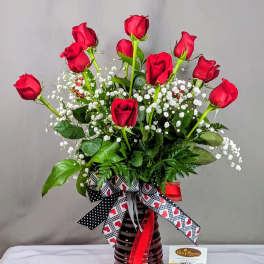 Red roses arranged in a dark glass vase with white baby's breath.