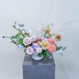 Pastel mixed flower arrangement in a white vase on a pedestal