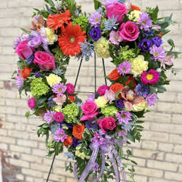 Heart-shaped floral wreath with pink roses and purple daisies on a stand
