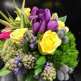 Bouquet of yellow roses and purple flowers in a low vase