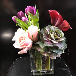 Mixed bouquet with pink roses, purple tulips, and a red calla lily in a glass vase