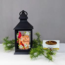 Black lantern with a memorial card and greenery on a white cloth