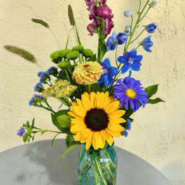 Mixed bouquet in a blue glass mason jar with a sunflower and blue flowers