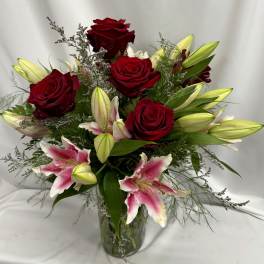 Red roses and lily buds arranged in a clear glass vase