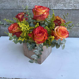 Orange-red roses in a square vase with yellow filler flowers