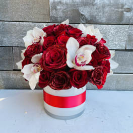 Red roses and white orchids in a white hat box with a red ribbon