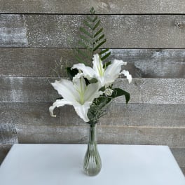 White lilies in a clear glass vase with greenery