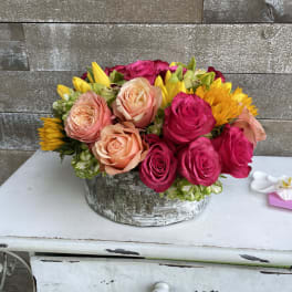 Mixed roses and sunflowers arranged in a rustic round container