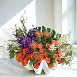Orange and purple floral arrangement in a white shell-shaped vase