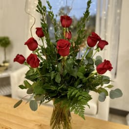 Red roses arranged in a clear glass vase with mixed greenery