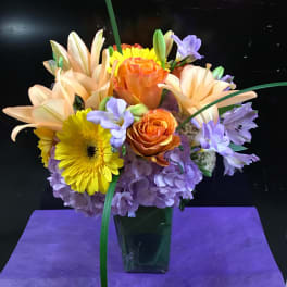 Mixed bouquet of orange, yellow, and lavender flowers in a glass vase