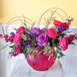 Pink and purple roses arranged in a round glass vase