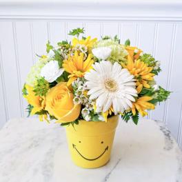 Yellow and white flower arrangement in a smiley-face pot