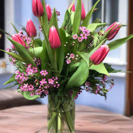 Pink tulips arranged in a clear glass vase with small pink blossoms