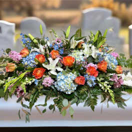 Large mixed floral casket spray with lilies, roses, and blue hydrangeas