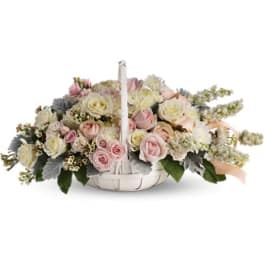 Basket arrangement of pink and white roses with a candle in the center