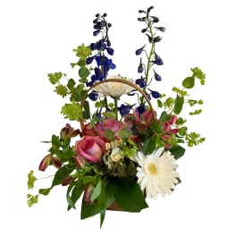 Basket arrangement with pink roses, white daisies, and blue flowers