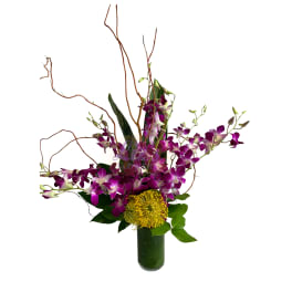 Purple orchids and a yellow pincushion bloom in a tall vase arrangement