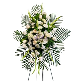 White funeral spray with roses, lilies, and daisies on palm fronds