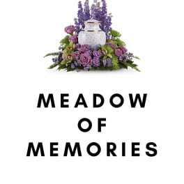 Purple floral arrangement around a white urn with "Meadow of Memories" text below