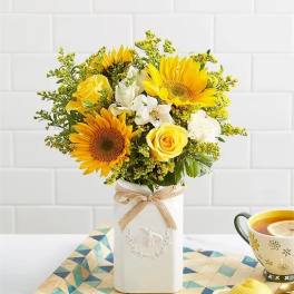 Yellow sunflowers and roses in a white vase with a ribbon