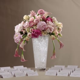 Tall glass vase of pink and white flowers on a table surrounded by name place cards.