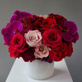 Red and pink roses with purple orchids in a white vase