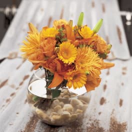 Orange and yellow flower arrangement in a clear glass bowl vase