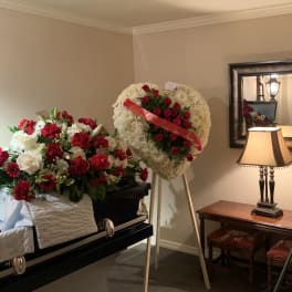 Two floral funeral tributes beside a casket, one on an easel and one draped over the casket.