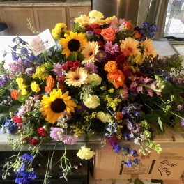 Large mixed flower arrangement with sunflowers, roses, and daisies on a table
