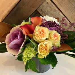 Bouquet of yellow roses, calla lilies, and purple blooms in a metal container